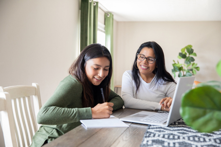 mother and daughter sitting at a table with a laptop